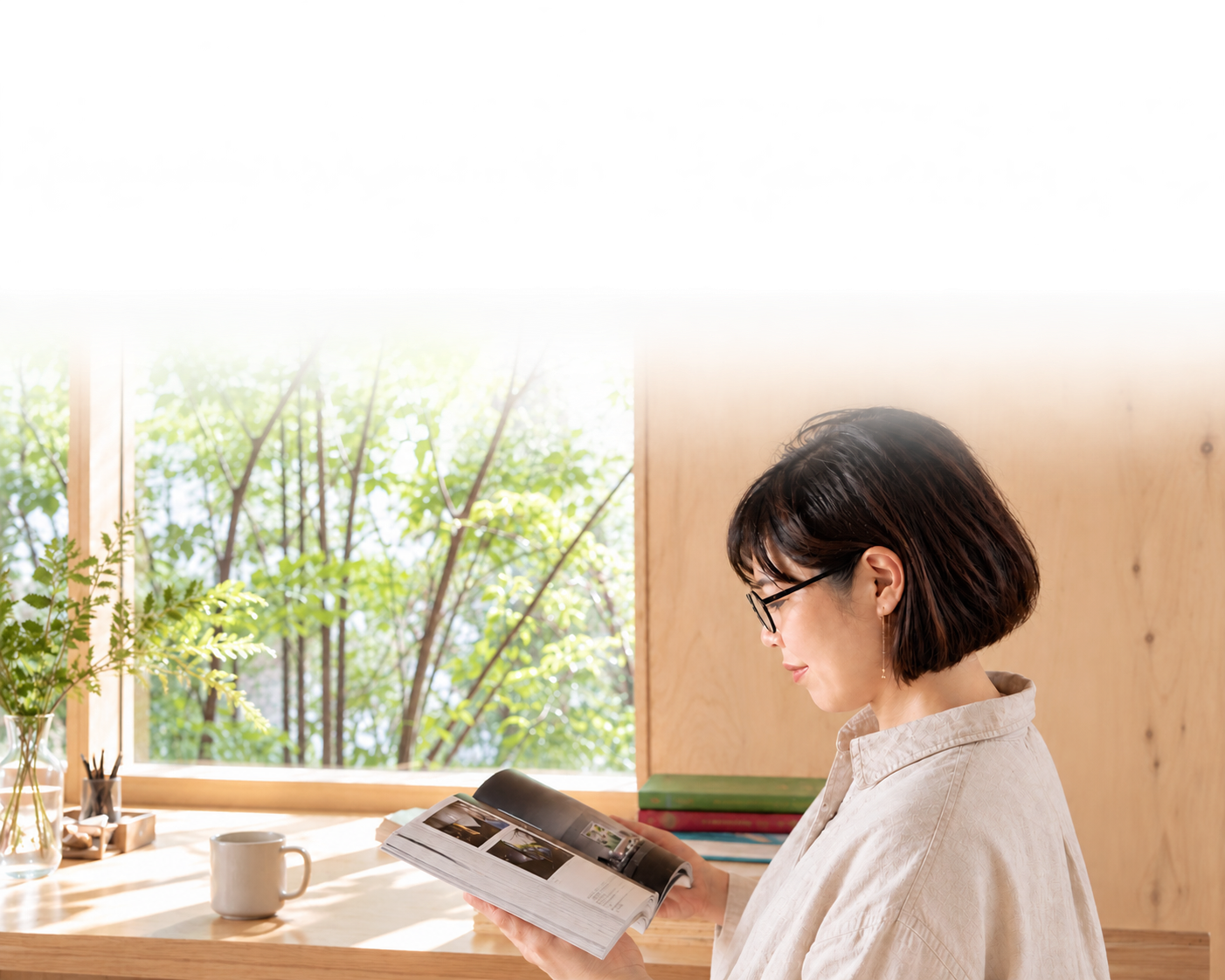 窓辺の緑を眺めながら、雑誌をめくる女性